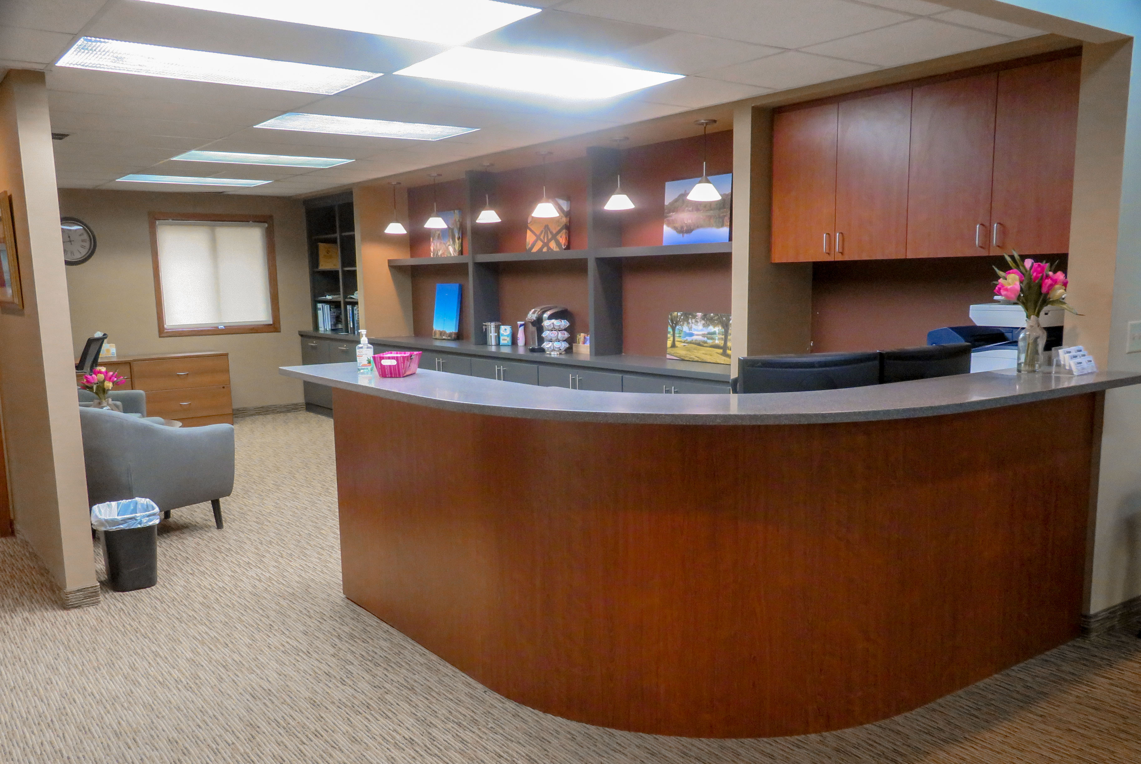 Photo of the remodeled reception area of the new building. Photo shows a desk and part of an alcove with chairs and items on the wall.